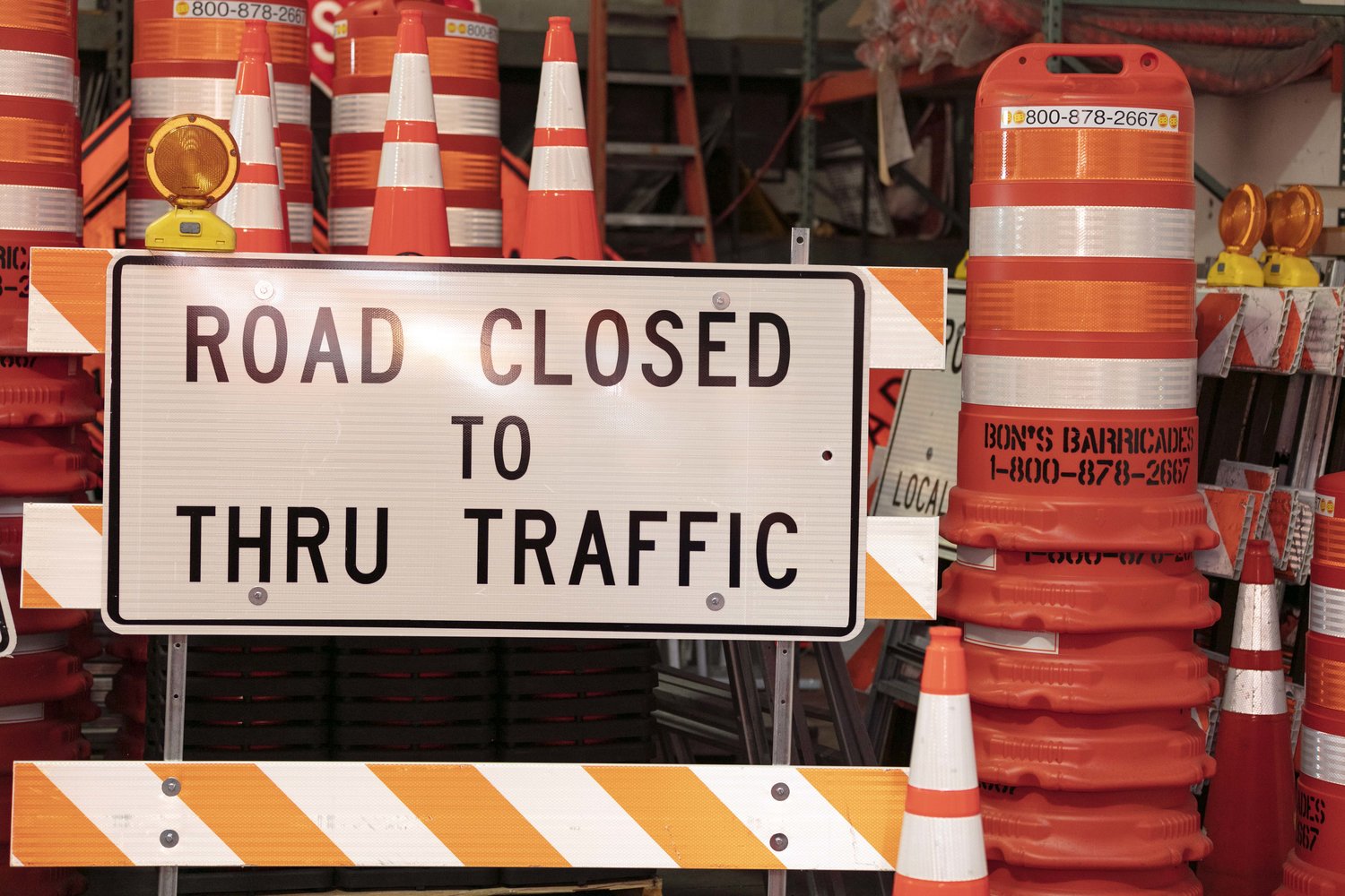 Plain “Road closed to thru traffic” signage in front of stacks of traffic cones and barricades